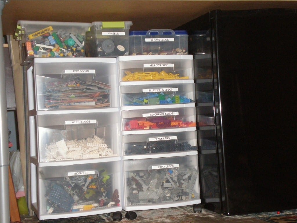 Legos Bins under a table next to a refrigerator