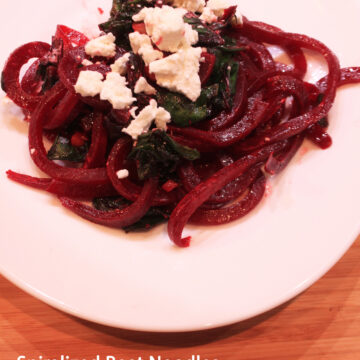 a white plate on a wood table - with the beet noodle dish on it. title of the post is at the bottom - pinterest image
