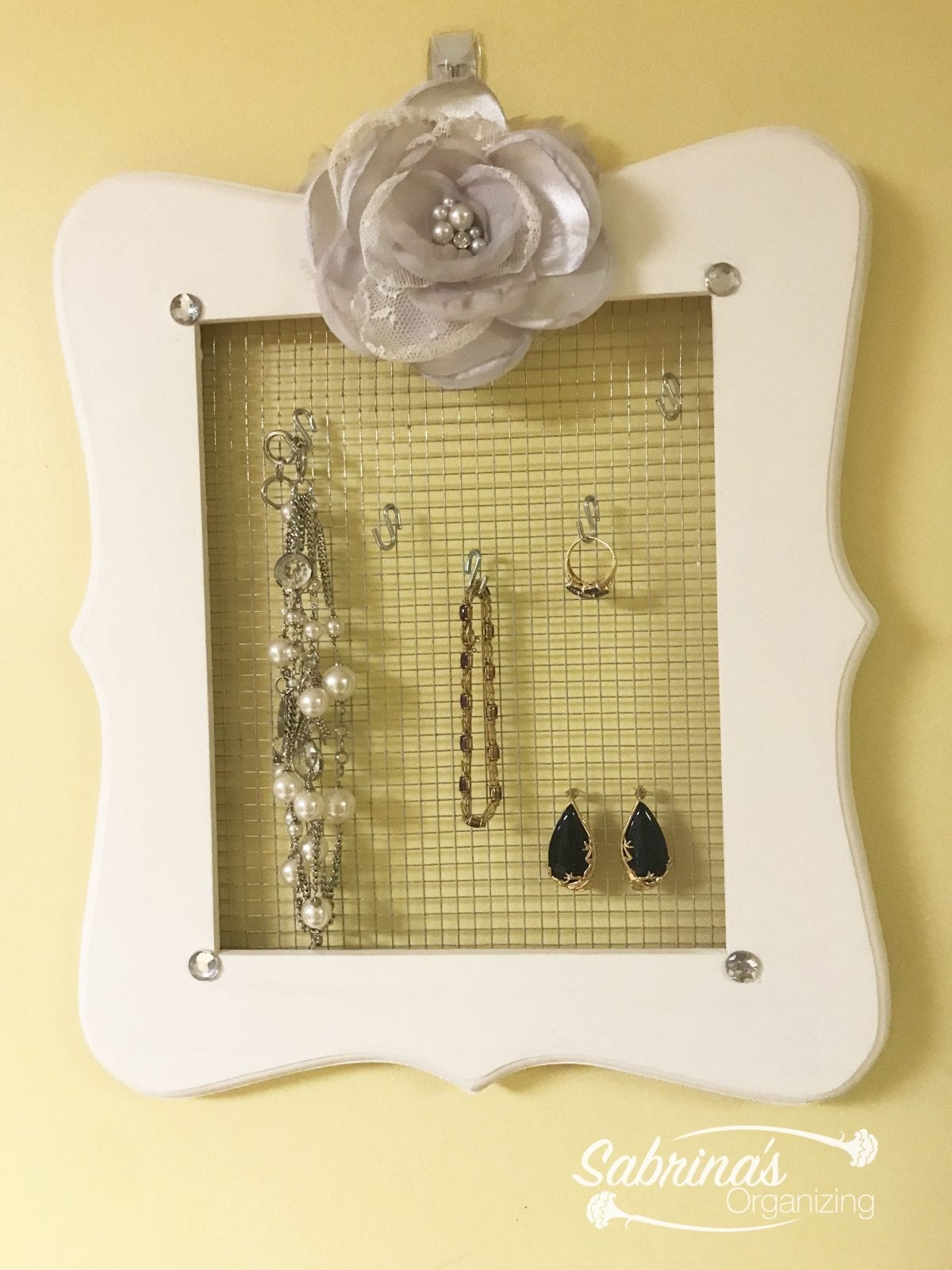 white picture frame with wire mesh hanging jewelry from it to organize and display pretty items