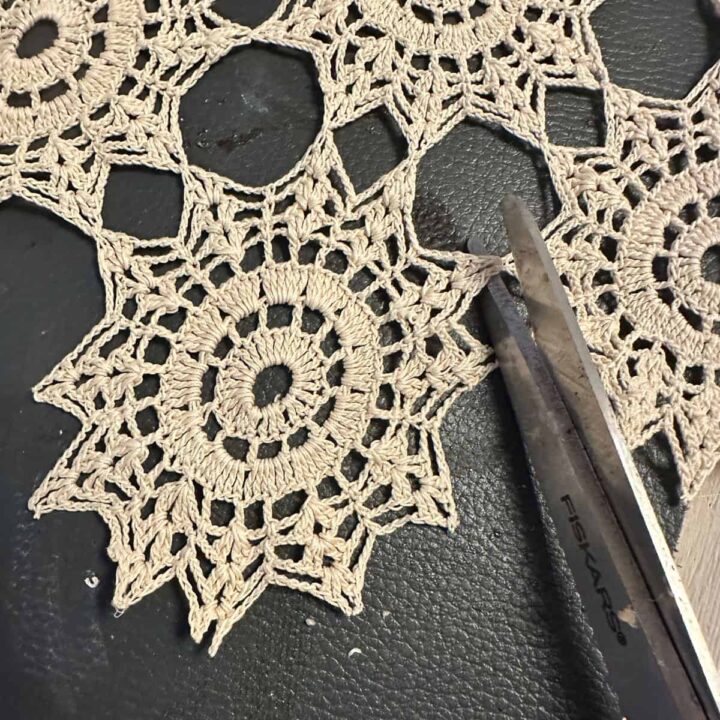 Scissors cutting out the crochet flowers from the runner - square image