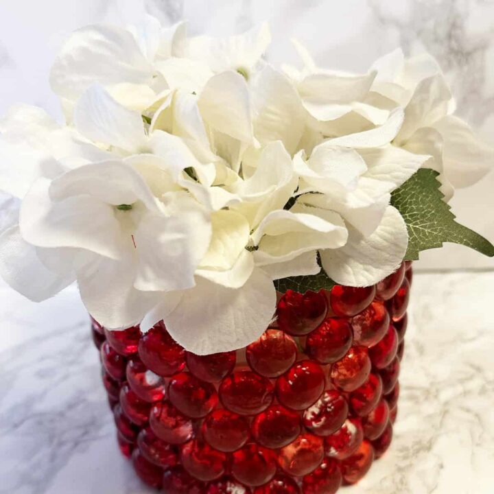 Glass red gem container with white poinsettia silk flowers inside