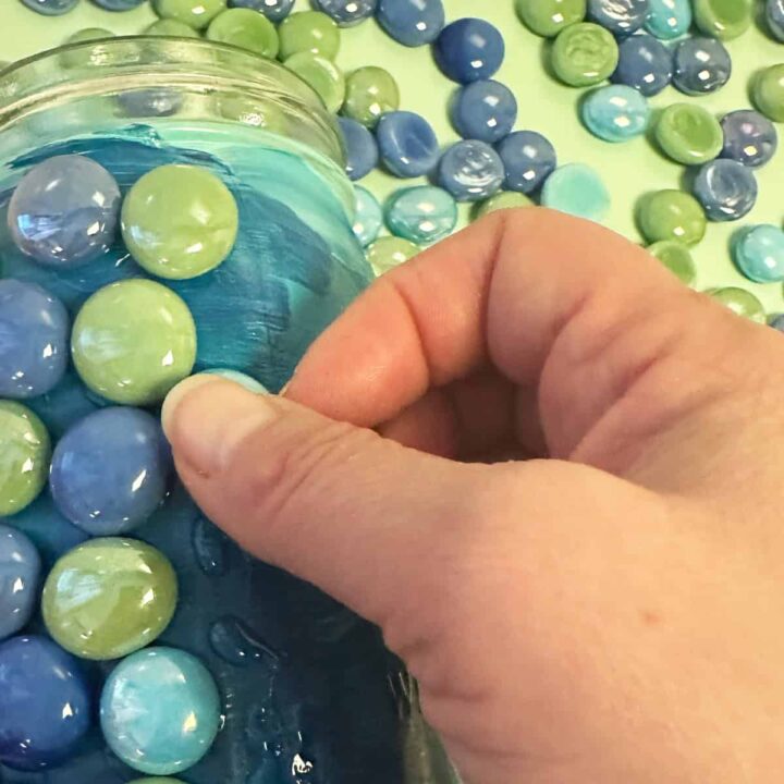 a hand adding the gems to the painted jar.