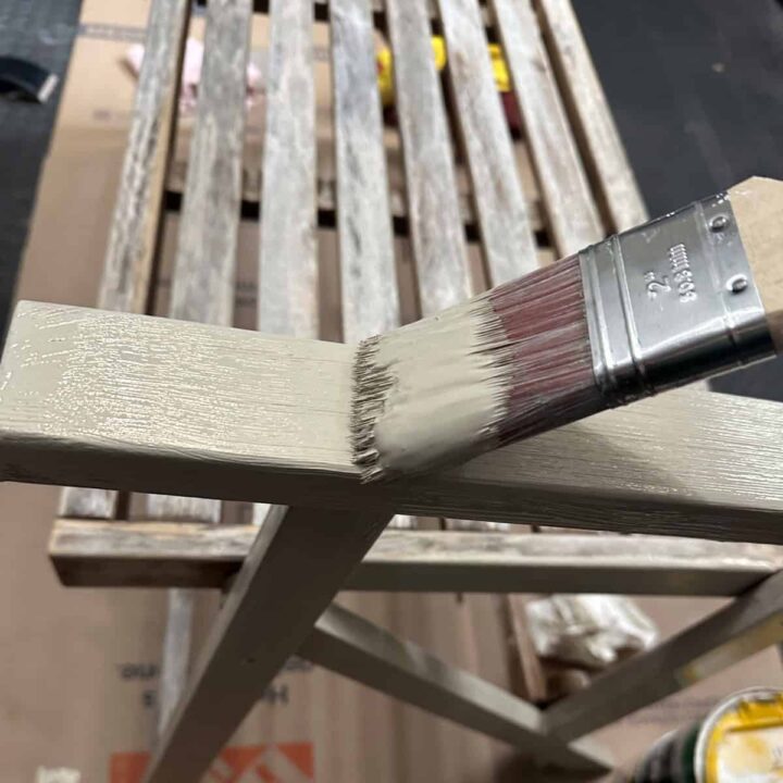 A paint brush and paint on the arm of the bench.