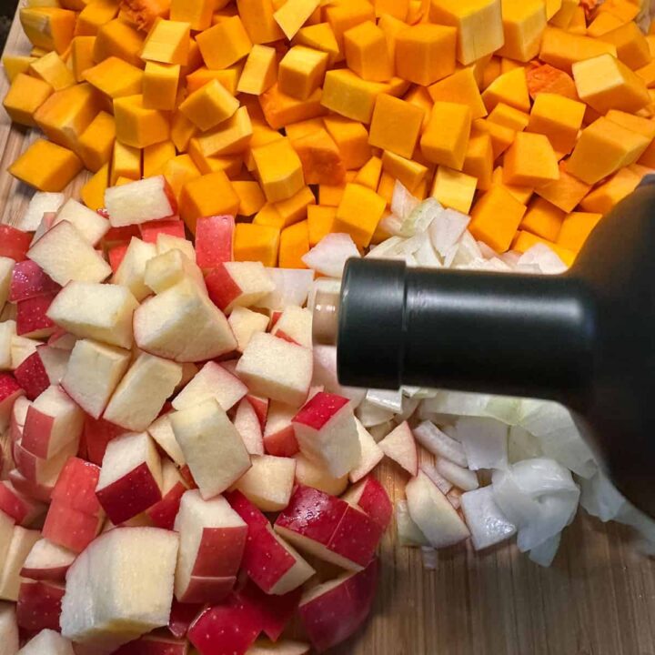 pouring olive oil over apples onions and butternut squash - square image