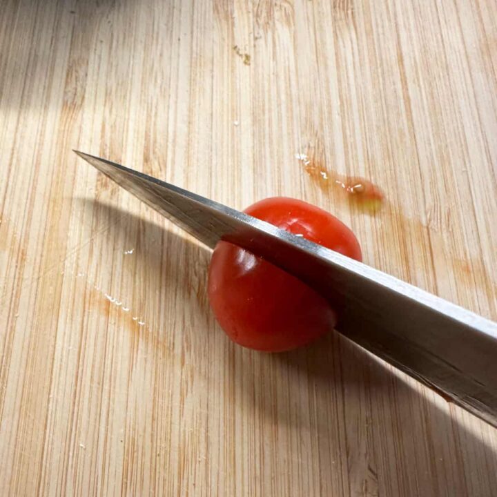 a knife cutting a cherry tomato on a cutting board - square image