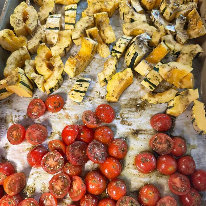 cut tomatoes at the bottom of the baking sheet and squash at the top with seasoning on them - square image