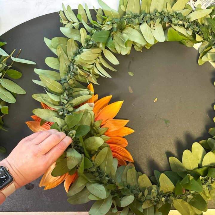 a hand is tying the sunflower to the wreath