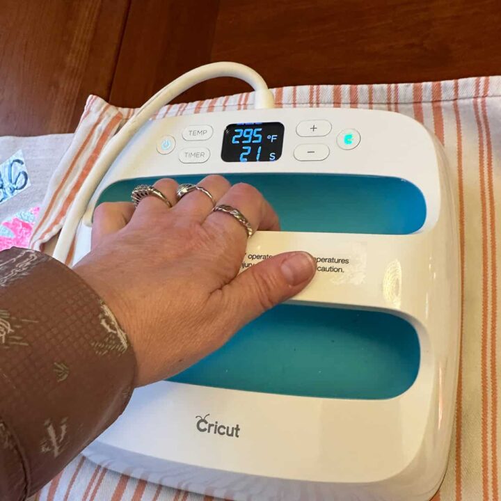 square image - showing my hand holding the Cricut heat press on cotton tea towel over the runner