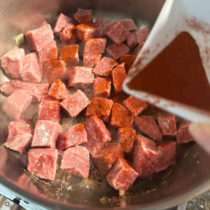 paprika poured over the raw meat in the sauce pan - square image