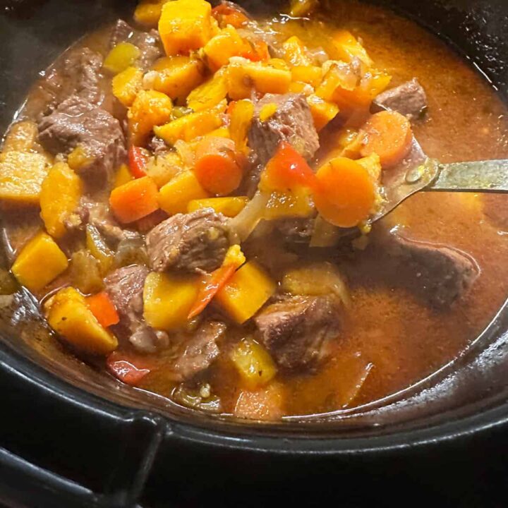 finished stew in the slow cooker - a spoon holding up some of it. square image