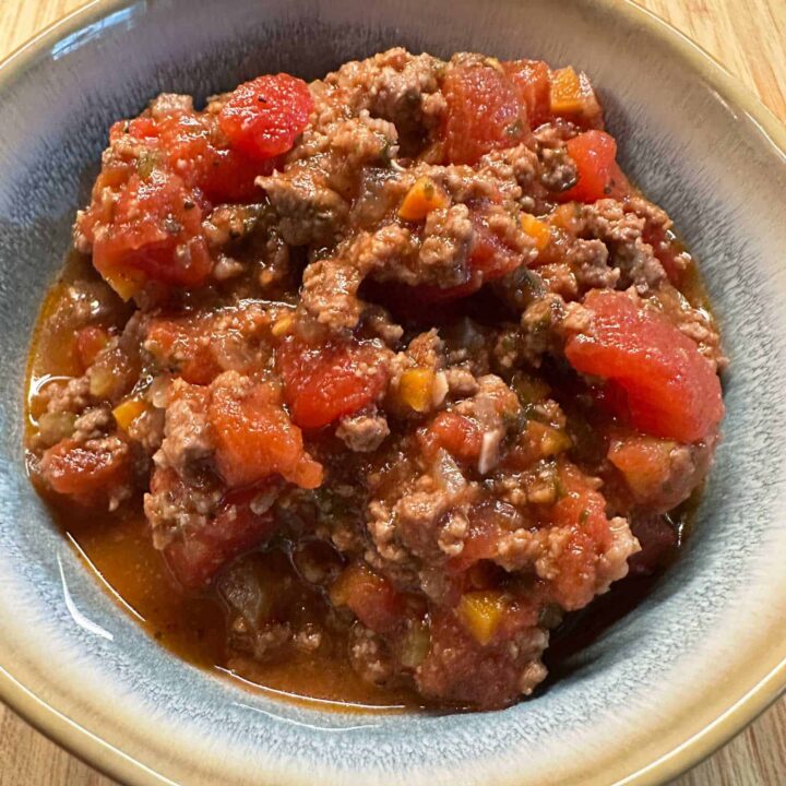cooked beef ragu in a bowl on a cutting board - square image