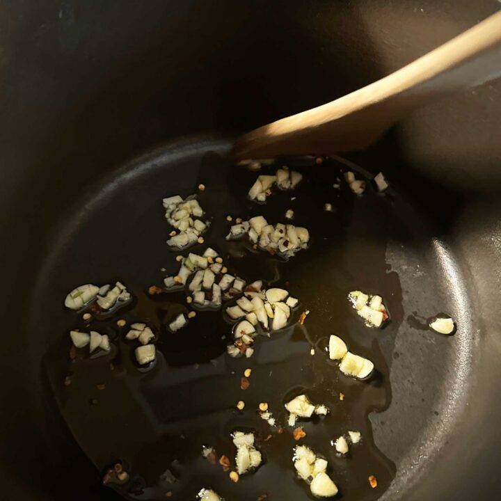 Garlic olive oil and red pepper flakes in a sauce pan with a wooden spoon - square image