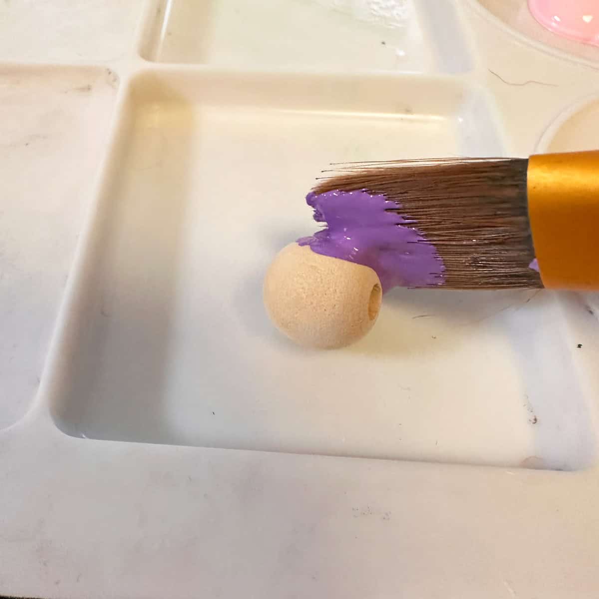 Paint the wooden beads to use as feet for the vitamin container - square image - paint brush touching the wooden bead with purple paint.