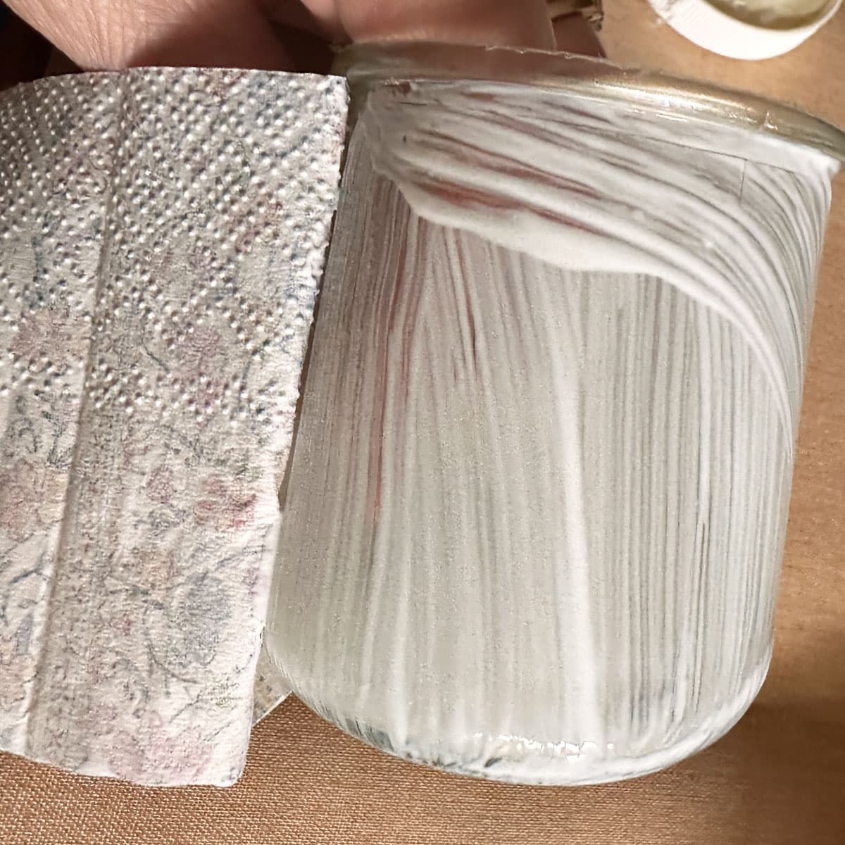 the glue on the jar laying the napkin over to adhere to it